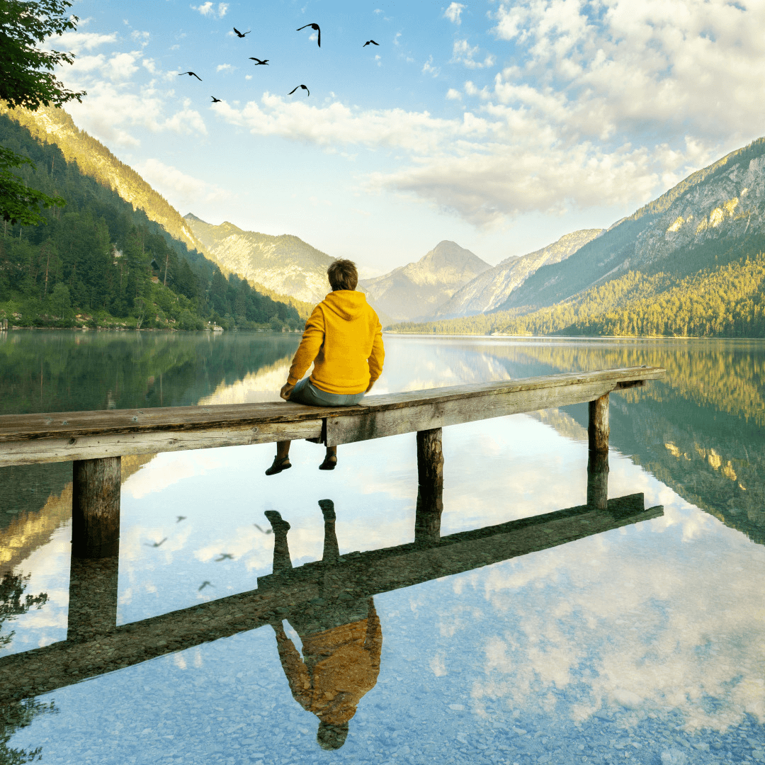 Junge mit gelber Jacke sitzt auf einem Holzsteg an einem Ufer und betrachtet die bergische Landschaft