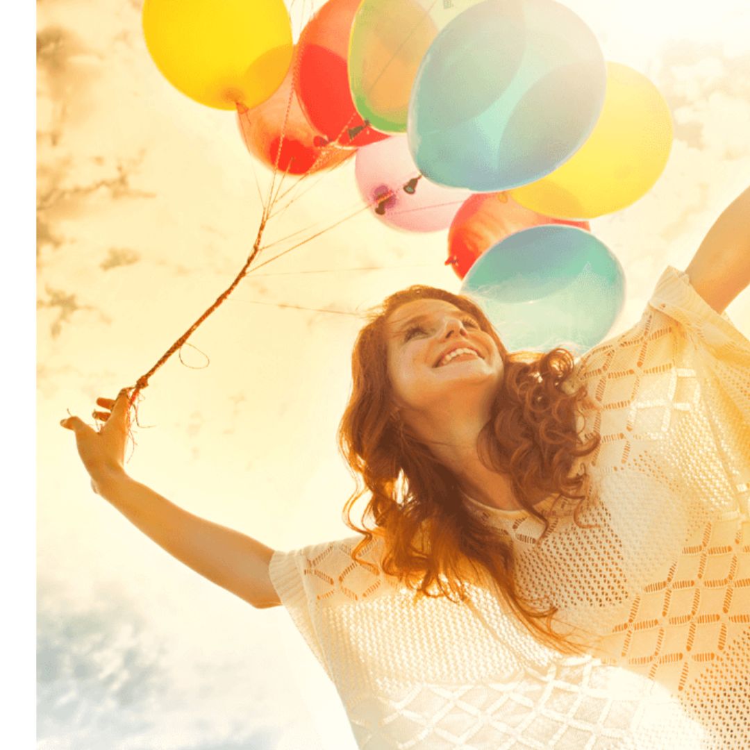 Eine Frau mit einem gelben Oberteil und mehreren bunten Ballons in der Hand steht auf einem Bein. Hinter hier der Himmel in gelb gefärbt.